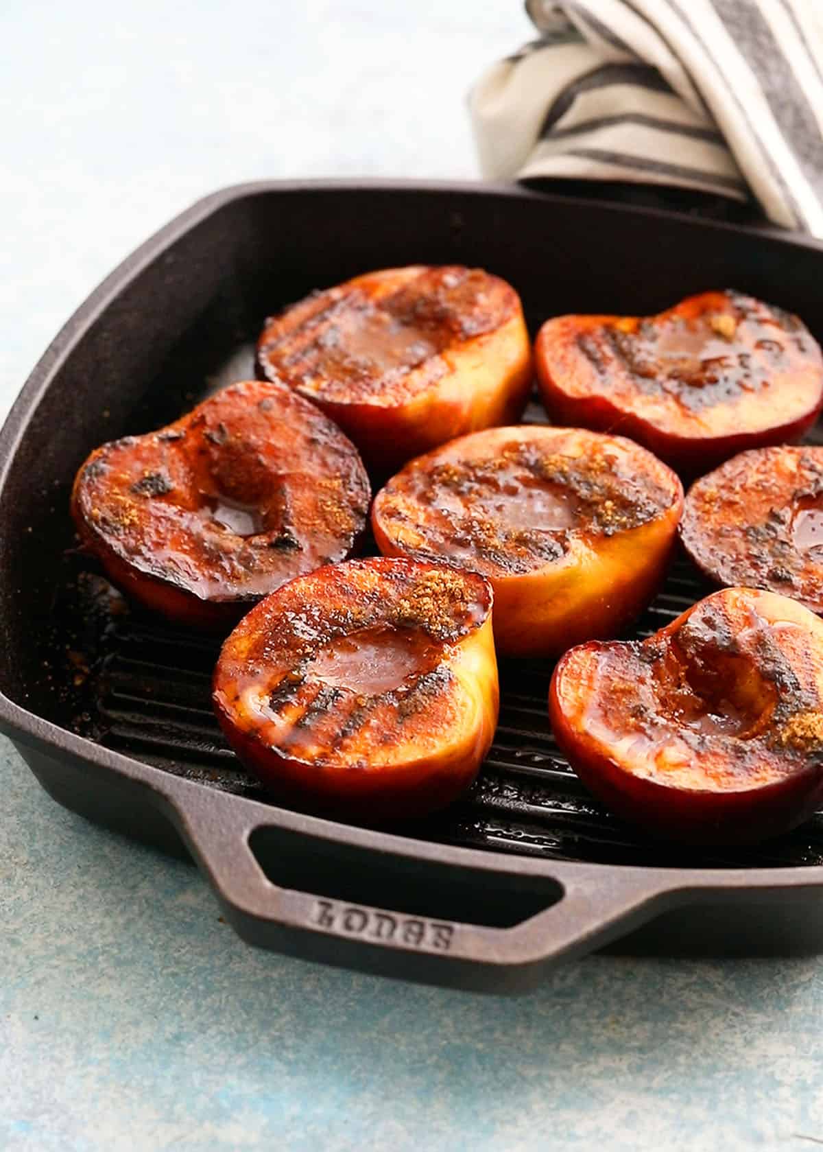 6 grilled peach halves placed in a grill pan.