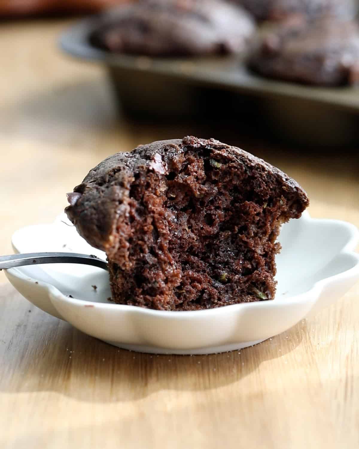 one brown chocolate zucchini muffin on a small white plate.