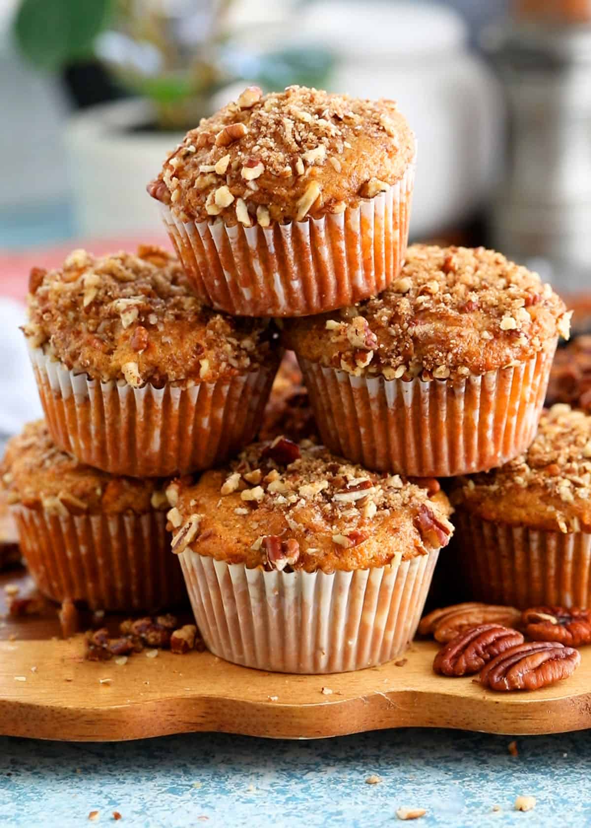 6 orange sweet potato muffins stacked on a brown board.