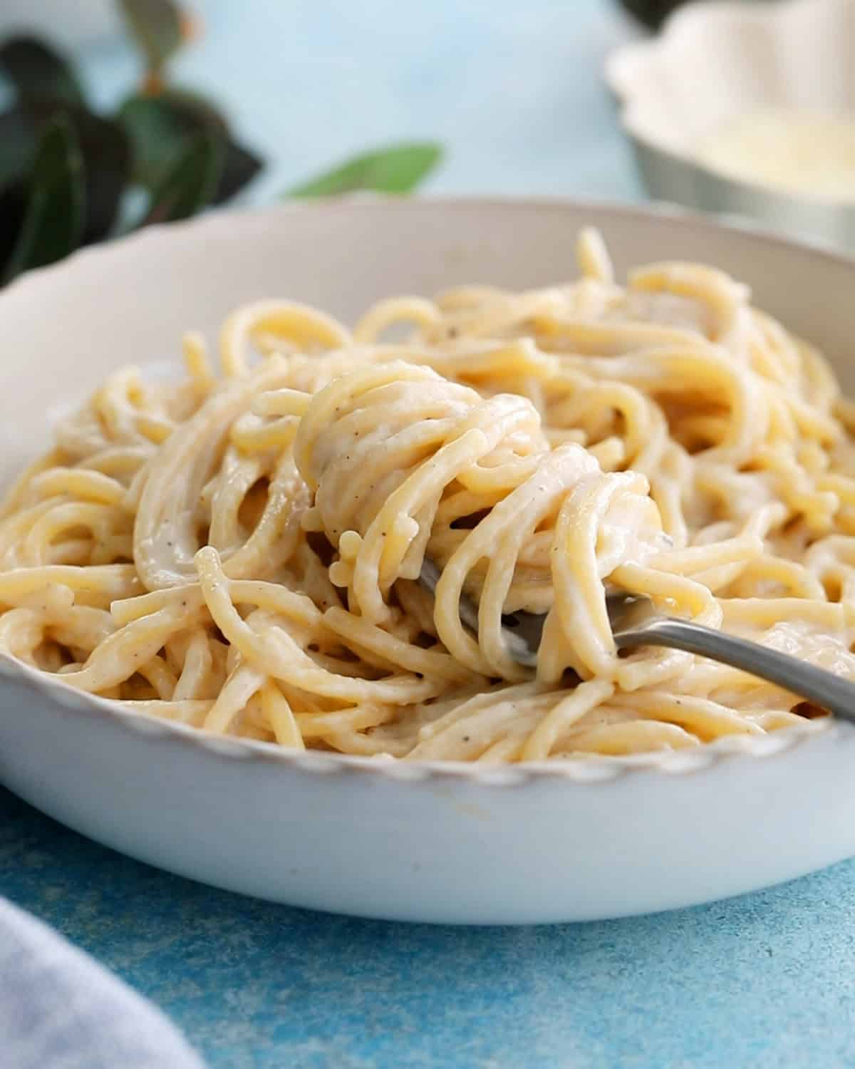 white alfredo pasta in a white bowl along with a black fork.