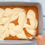 white cream cheese swirls over orange pumpkin cake.
