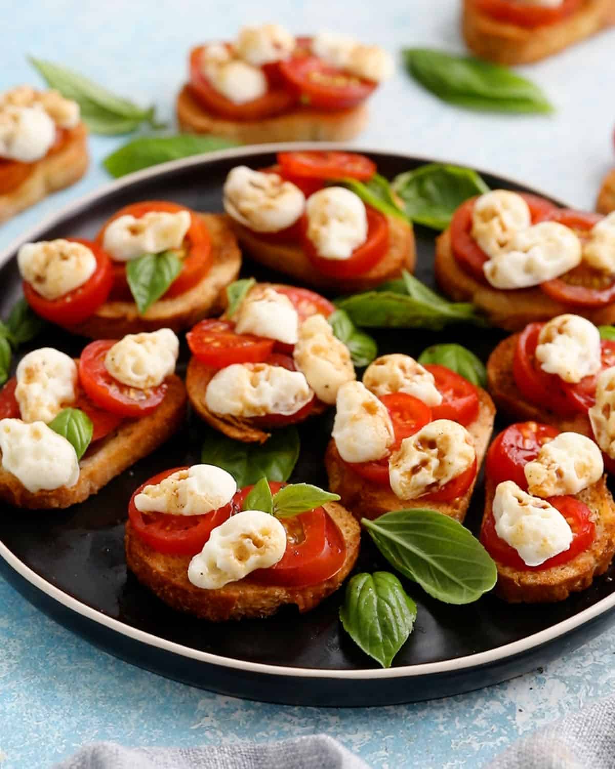 caprese toasts on black plate for Halloween appetizer.