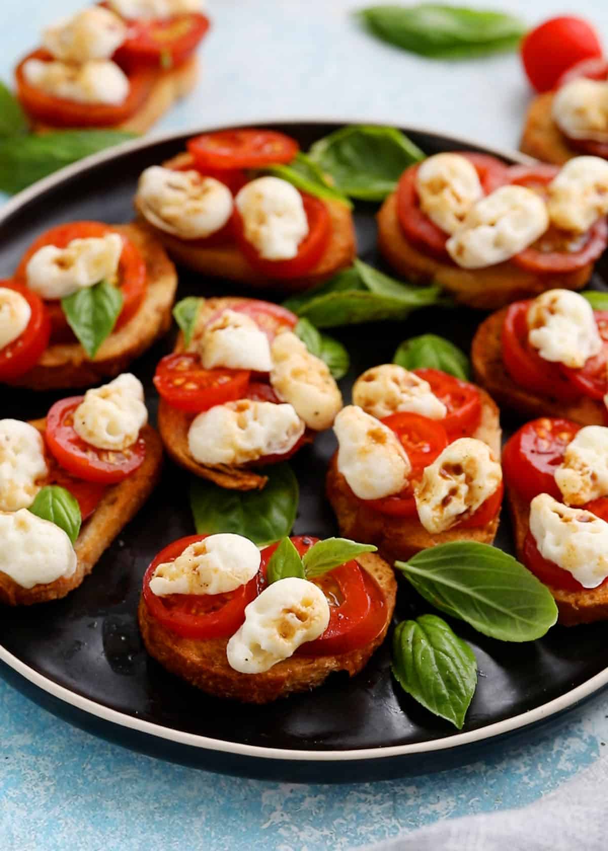 caprese toasts on black plate for Halloween appetizer.