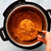 a hand holding one ladle filled with orange mashed sweet potatoes.