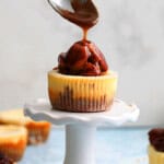 a hand pouring brown caramel sauce over one pecan cheesecake.