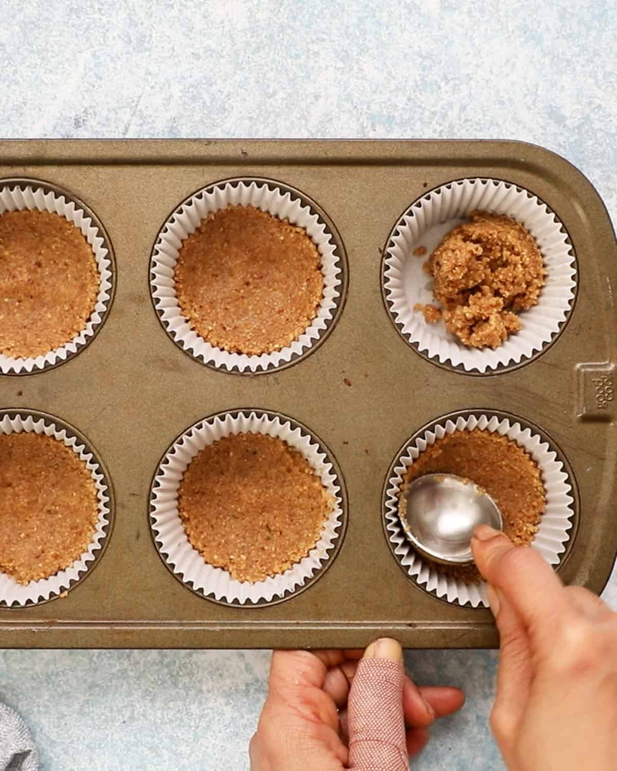 two hands pressing brown crust into a paper lined muffin pan.