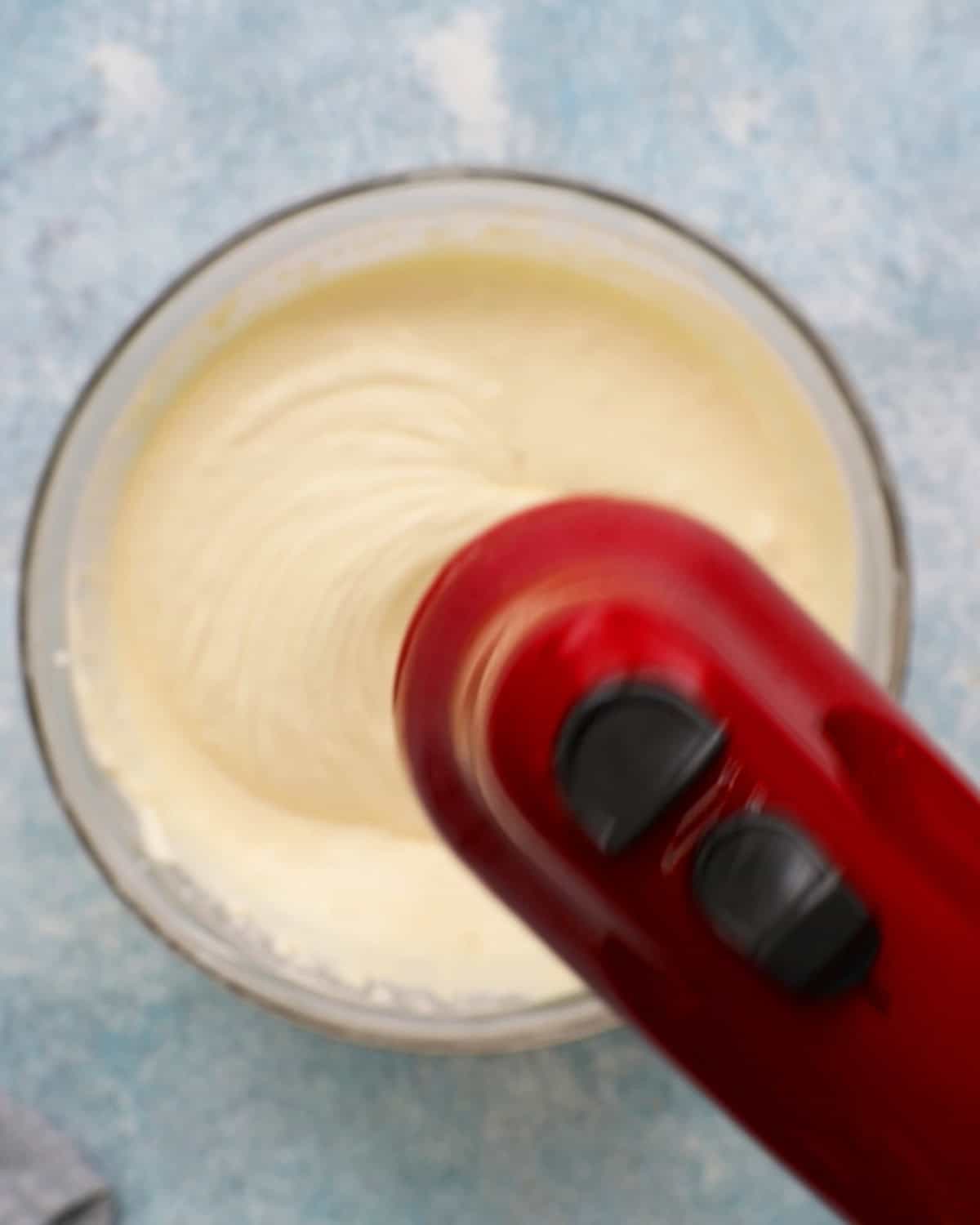 a red beater beating white cheesecake mixture.