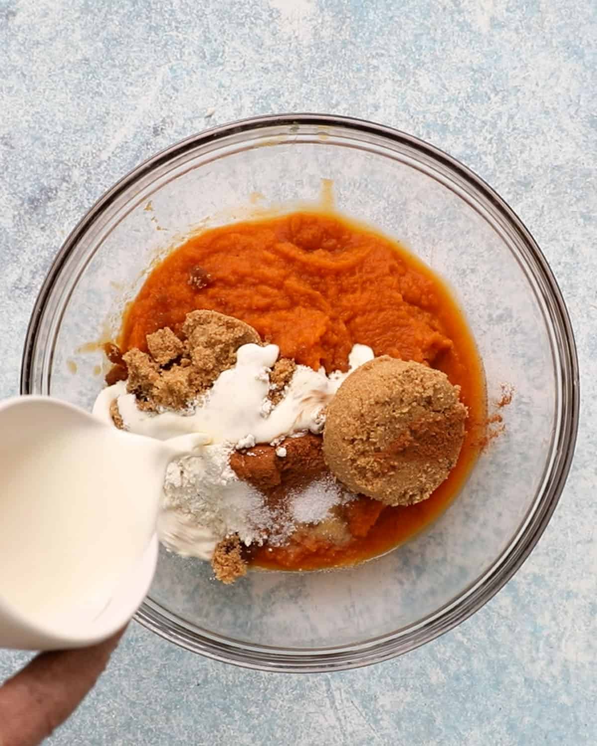 a hand pouring white cream into a glass bowl with pumpkin. 