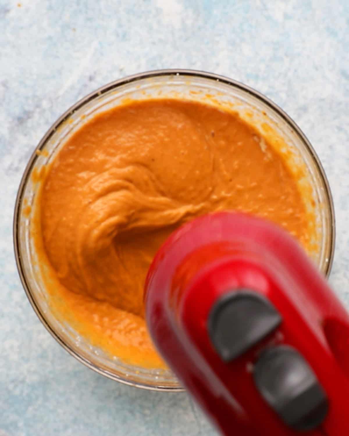 a red beater beating orange pumpkin filling. 