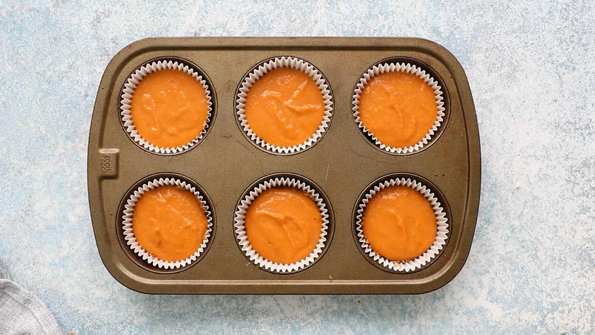 one 6 cup metal muffin pan filled with orange pumpkin batter.