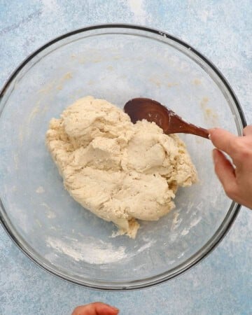 two hands mixing biscuit dough in a large glass bowl.