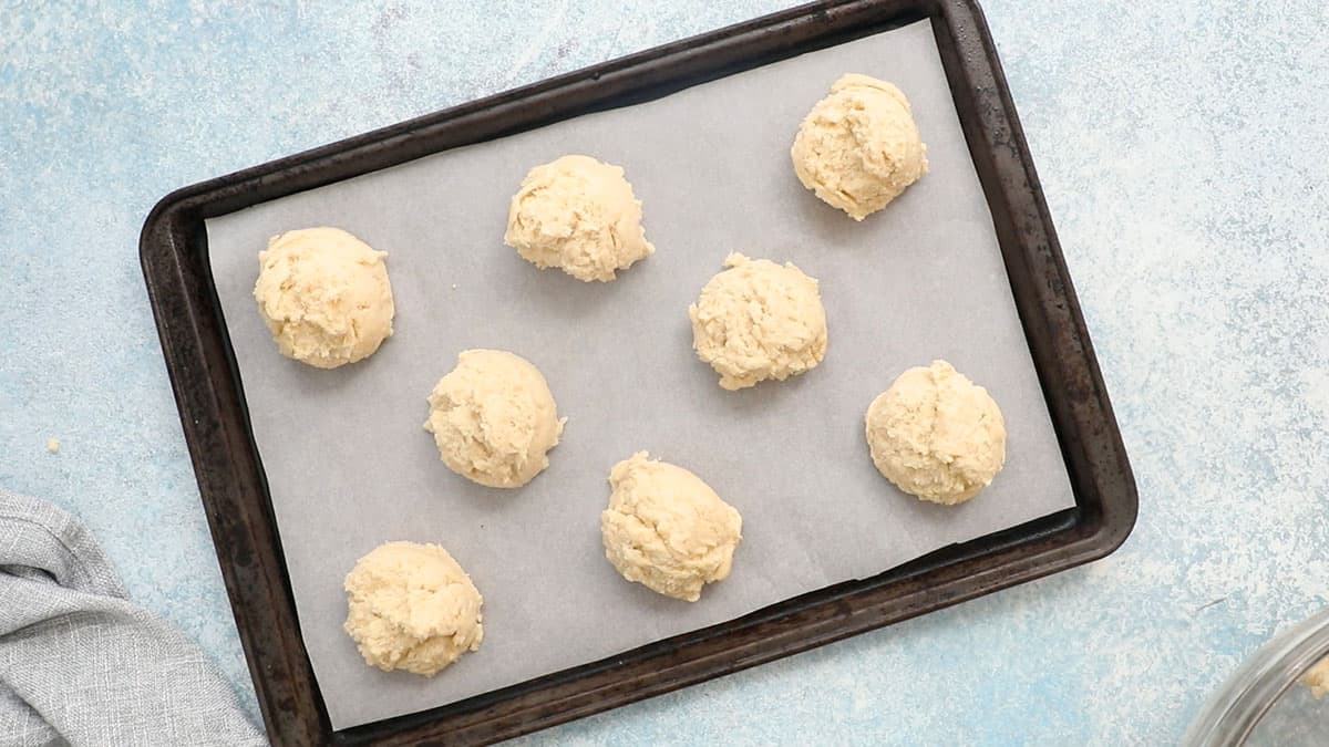 scoops of biscuit dough in a parchment lined baking sheet.