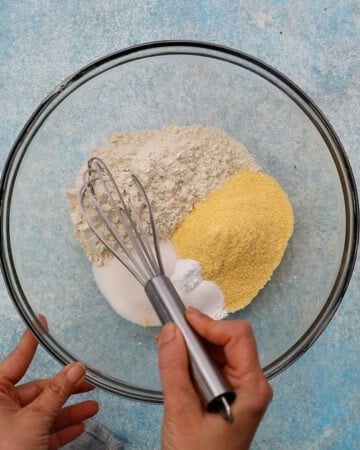 two hands whisking white and yellow flours in a glass bowl.