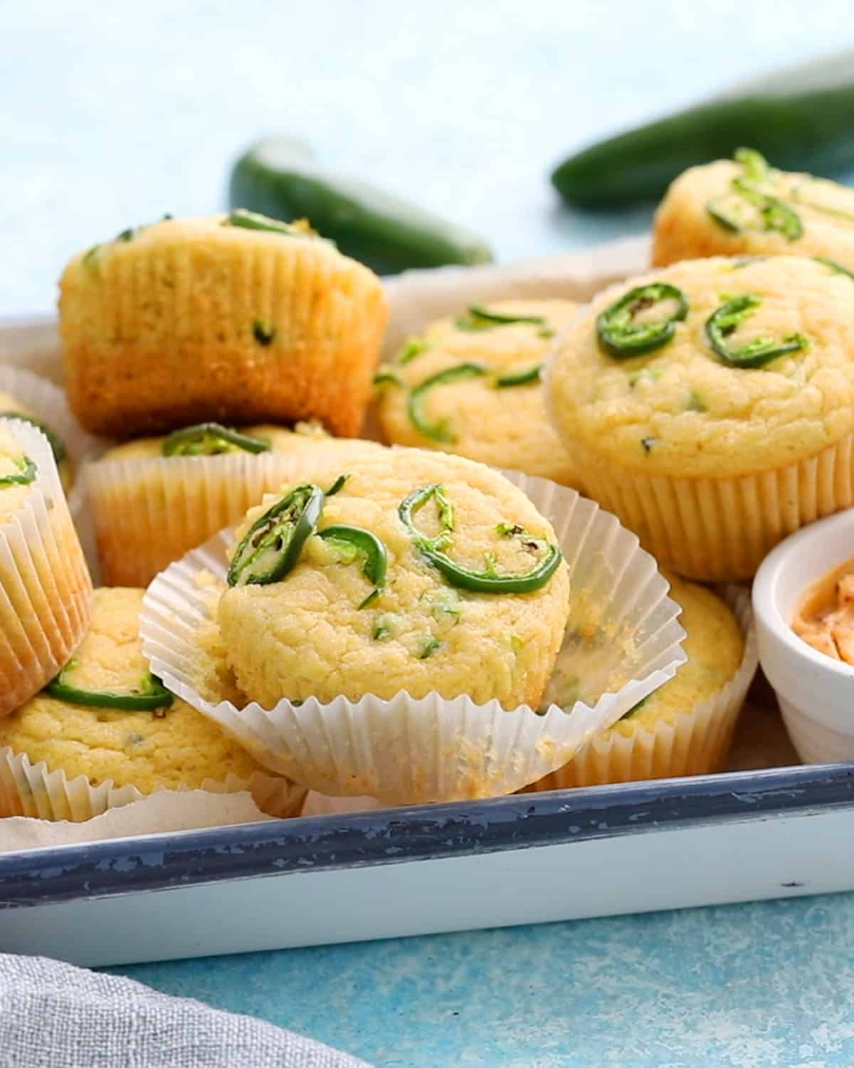 yellow cornbread muffins topped with green jalapeno slices in a white tray.