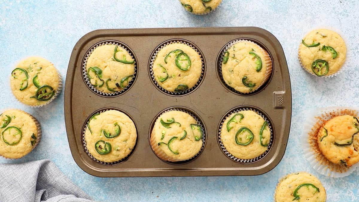 one metal muffin pan filled with baked yellow corn muffins topped with green jalapeno slices.