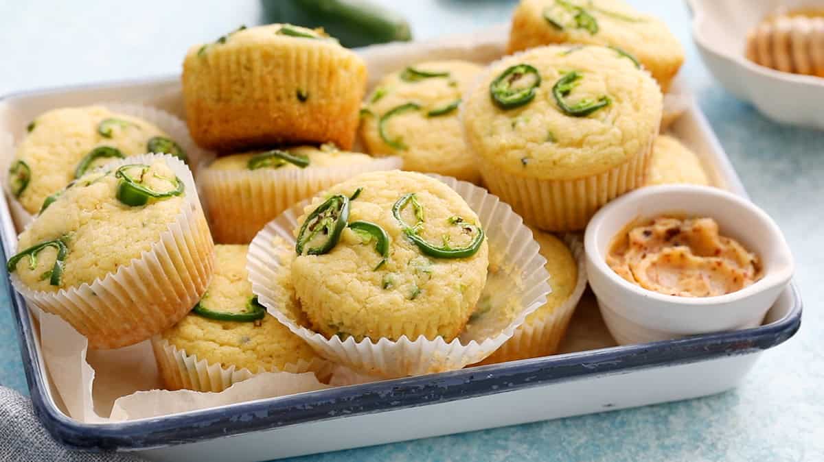 yellow cornbread muffins topped with green jalapeno slices in a white tray.