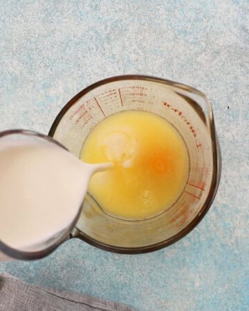 a hand pouring white buttermilk into a glass measuring cup.