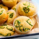 yellow cornbread muffins topped with green jalapeno slices in a white tray.