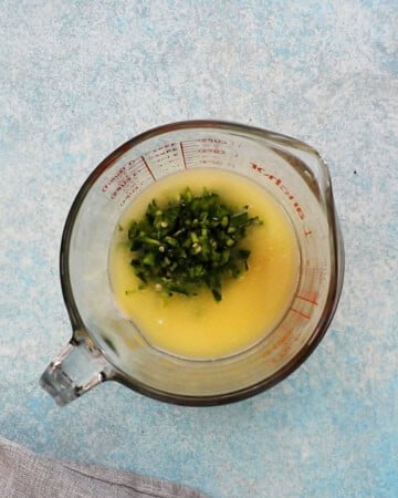 yellow liquid and chopped green peppers in a glass measuring cup.