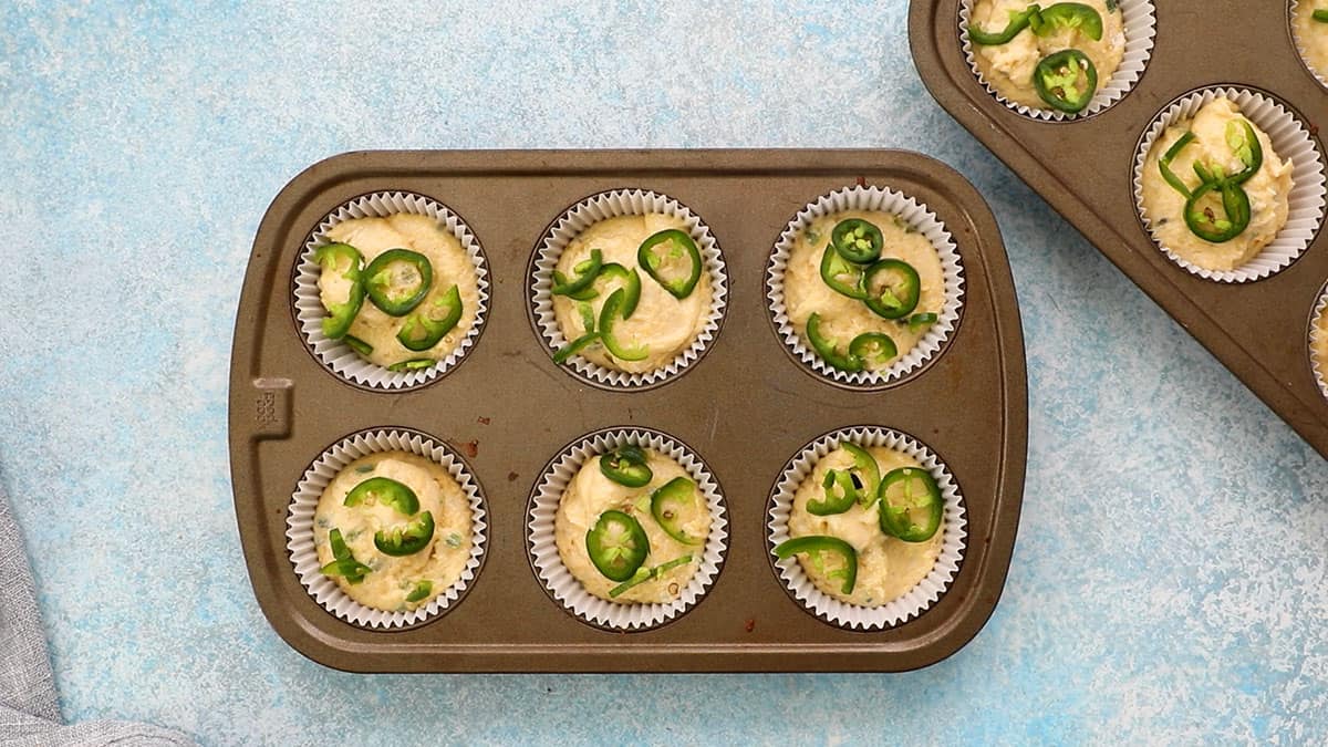 one metal muffin pan filled with yellow corn muffin batter topped with green jalapeno slices.