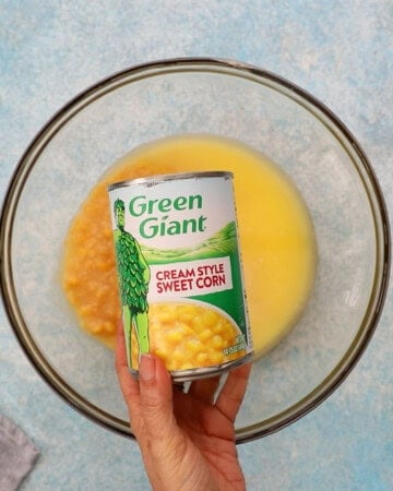 a hand holding one can of cream style sweet corn.