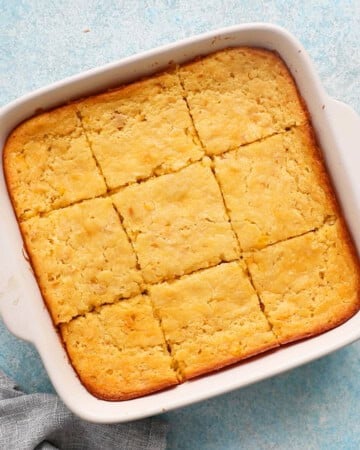 9 squares of baked corn casserole in a white baking dish.