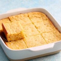 9 squares of baked corn casserole in a white baking dish.