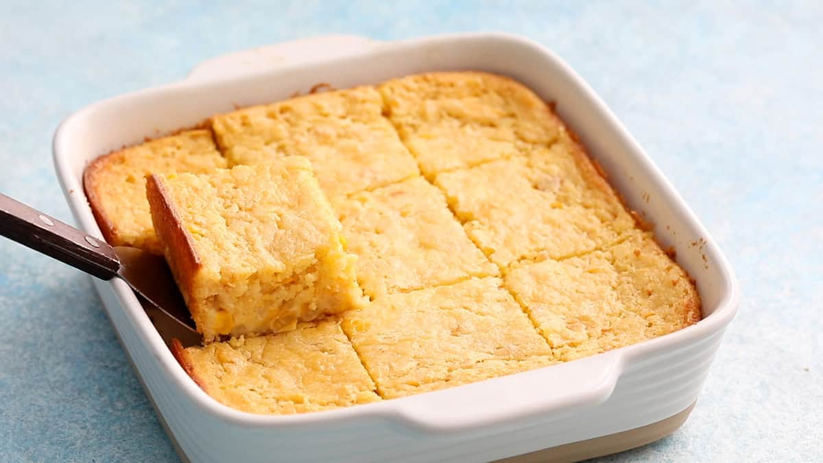 9 squares of baked corn casserole in a white baking dish.