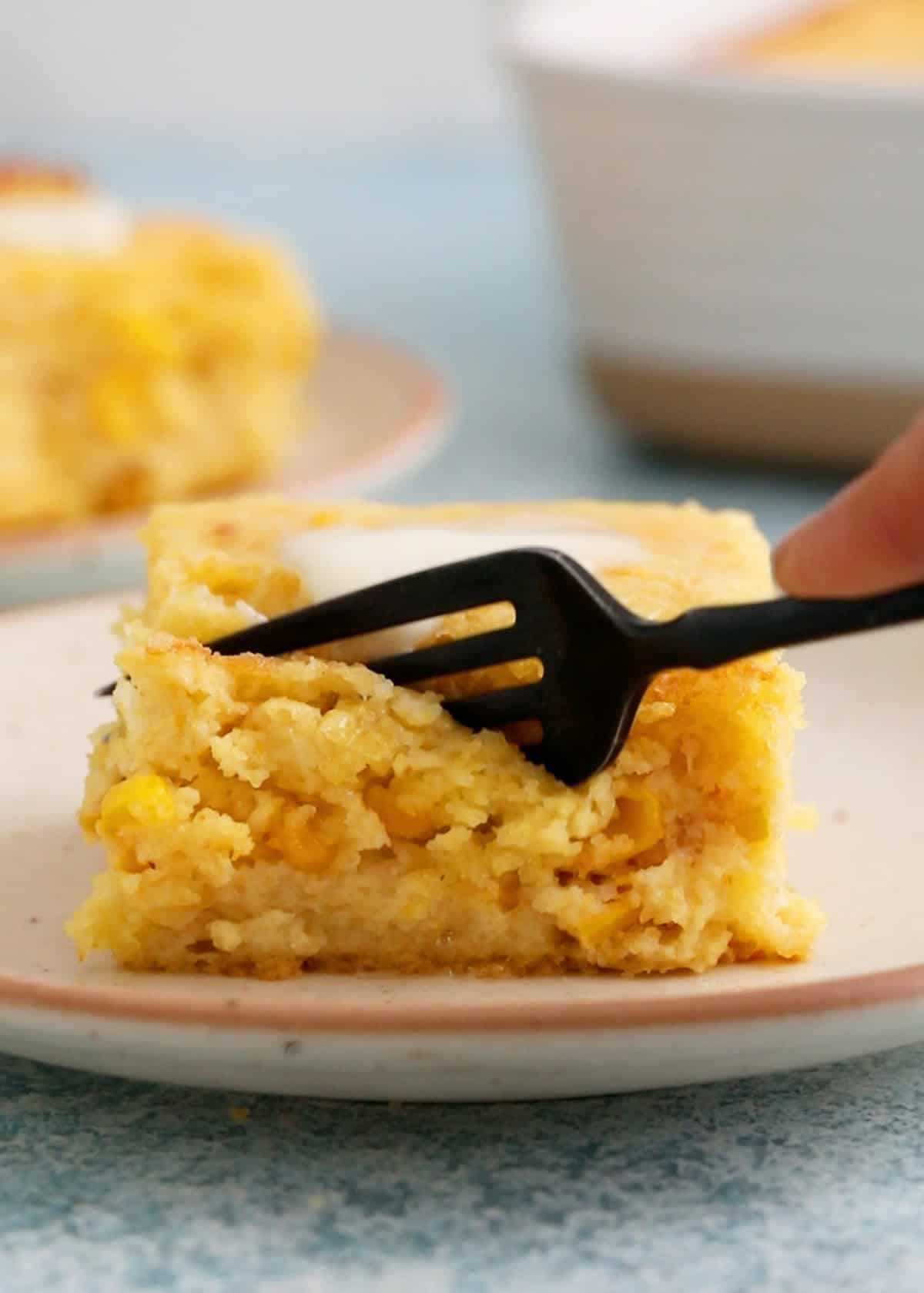 a black fork cutting one square slice of yellow corn casserole.