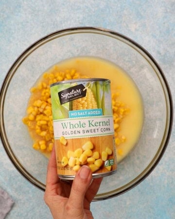 a hand holding one can of sweet corn.