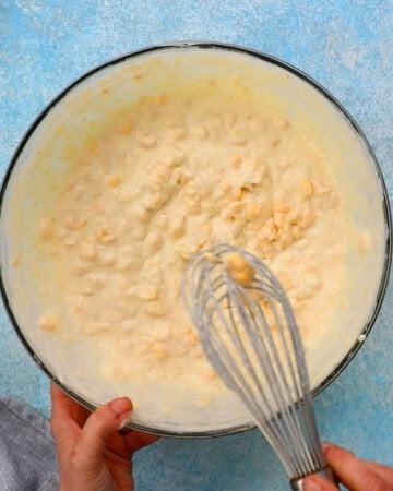 two hands whisking corn casserole mixture in a large glass bowl.