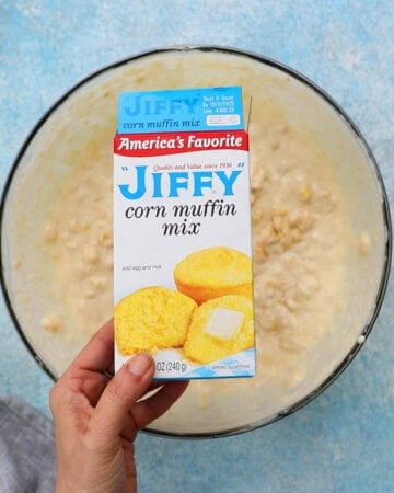 a hand holding one box of Jiffy corn mix.