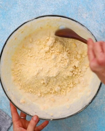 two hands mixing corn casserole batter in a large glass bowl.