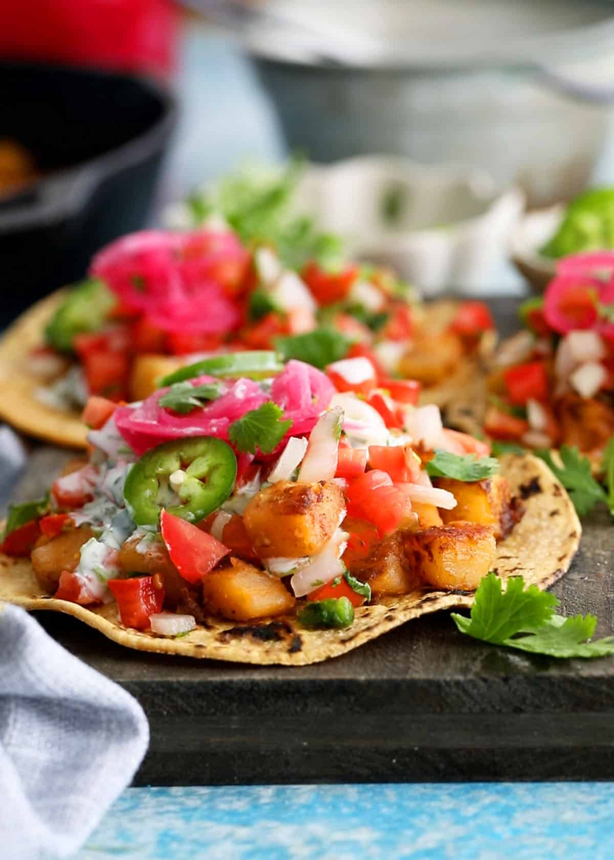 3 yellow potato tacos on a balck board.