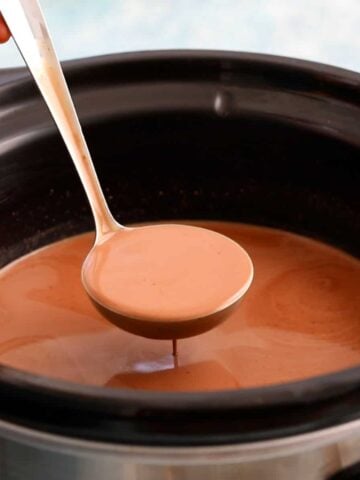 one ladle full of brown hot chocolate above a slow cooker.