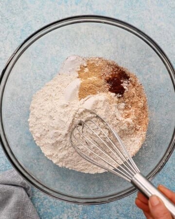a hand whisking flour in a glass bowl.
