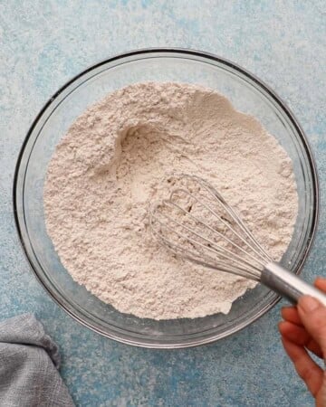 a hand whisking flour in a glass bowl.