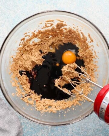 a red beater beating dark molasses and brown sugar in a large glass bowl.