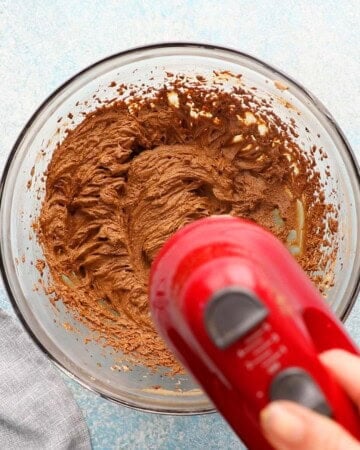 a red beater beating dark molasses and brown sugar in a large glass bowl.
