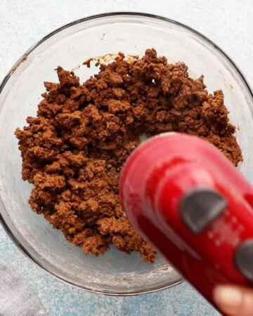 a red beater beating gingerbread cookie dough in a glass bowl.