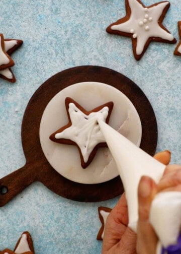 a hand icing a star shaped gingerbread cookie.