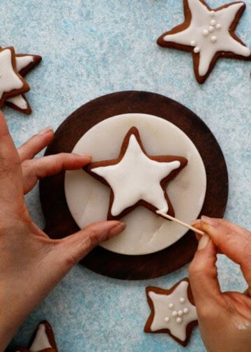 a hand icing a star shaped gingerbread cookie.