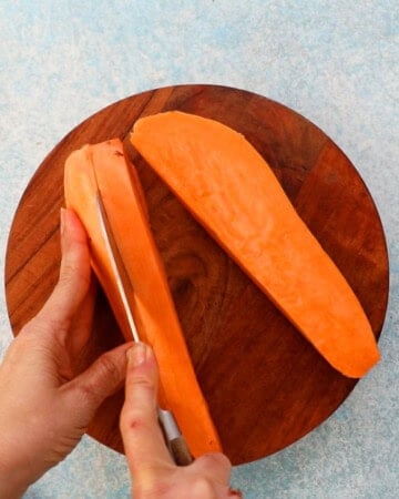 two hands cutting one orange sweet potato using a knife.