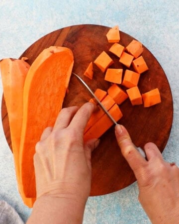 two hands cutting one orange sweet potato using a knife.