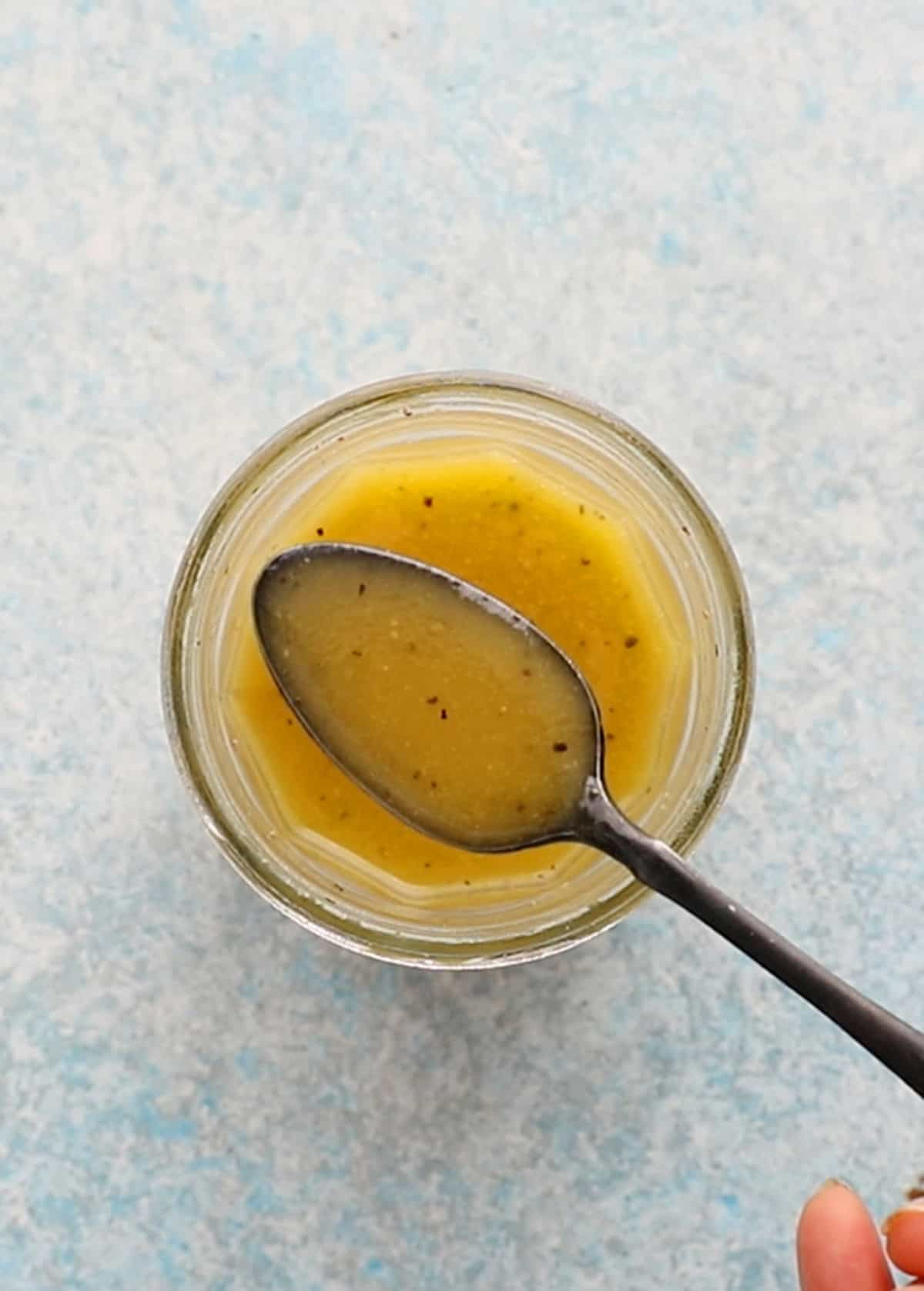 a hand holding one black spoon with yellow salad dressing.