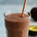 one brown avocado banana smoothie in a glass along with a brown straw.
