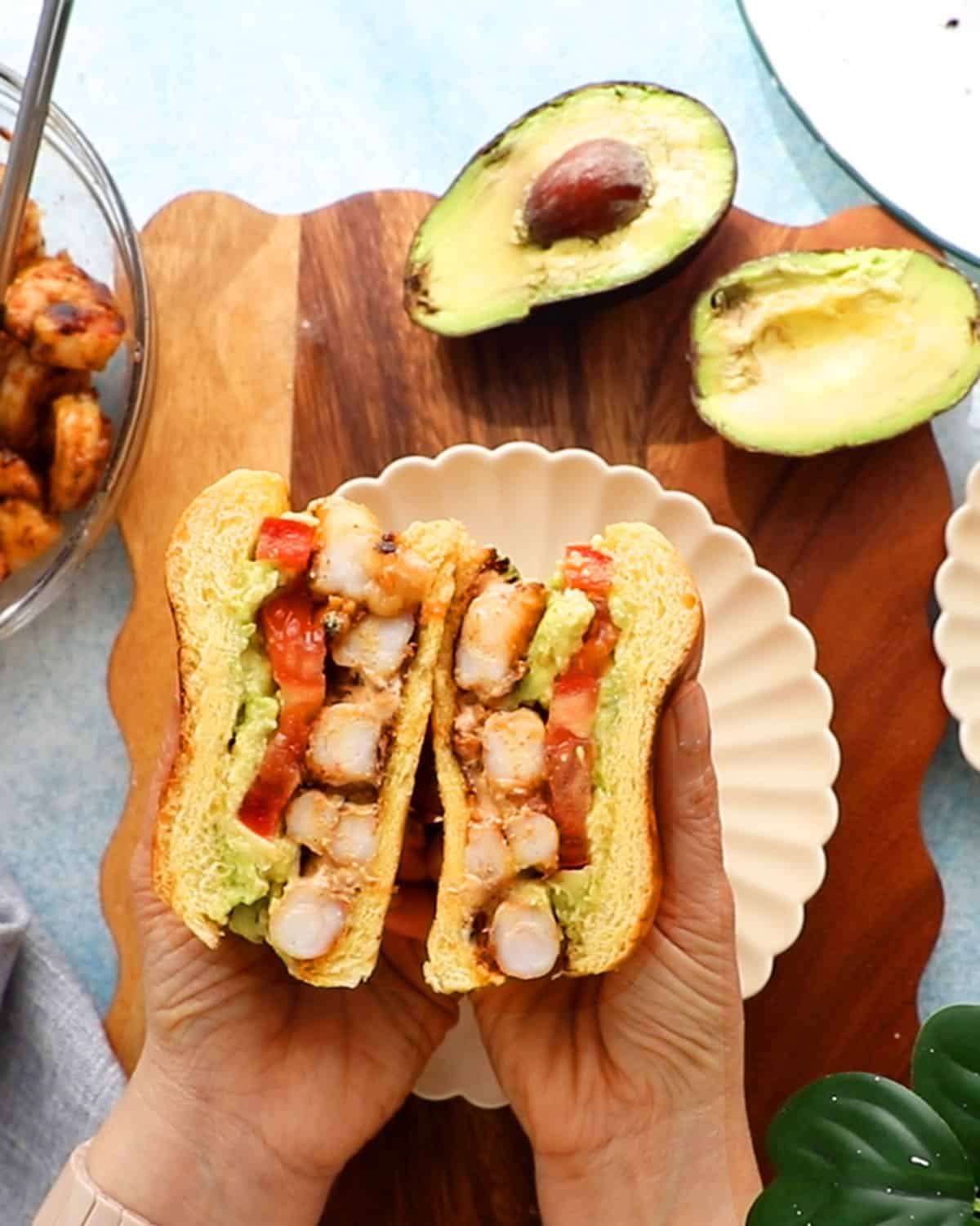 two hands holding two halves of a shrimp sandwich.