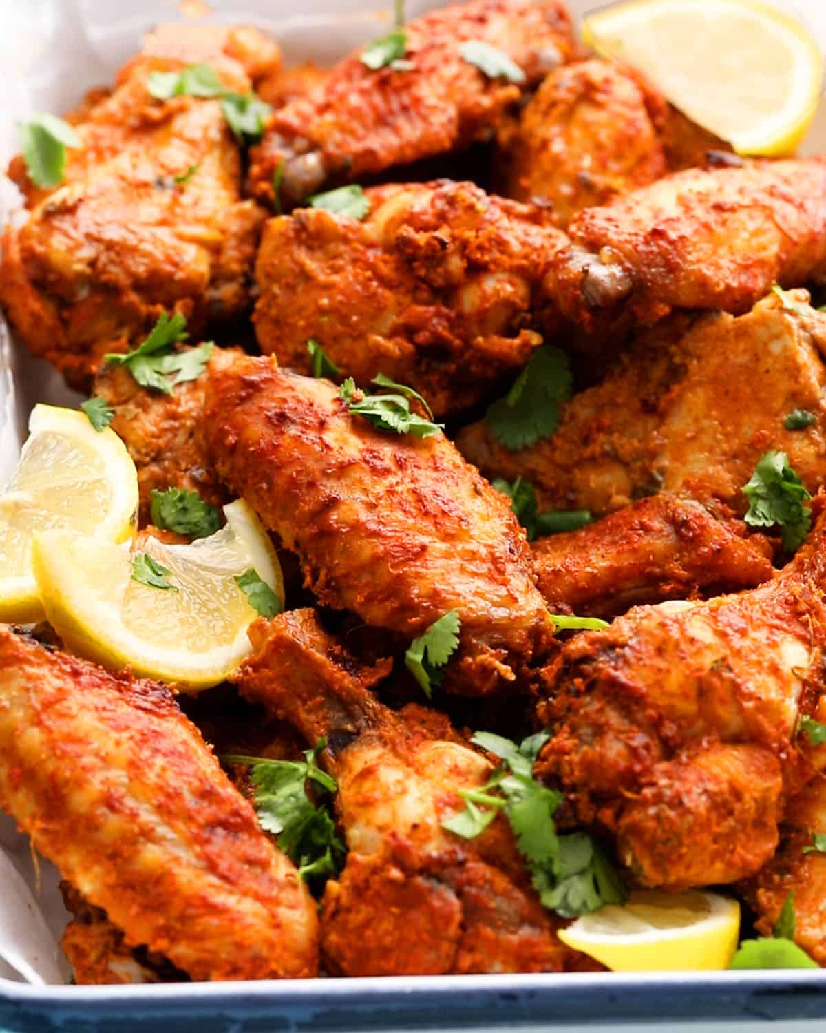 red colored tandoori chicken wings piled in a white plate.