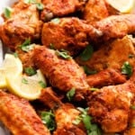 red colored tandoori chicken wings piled in a white plate.