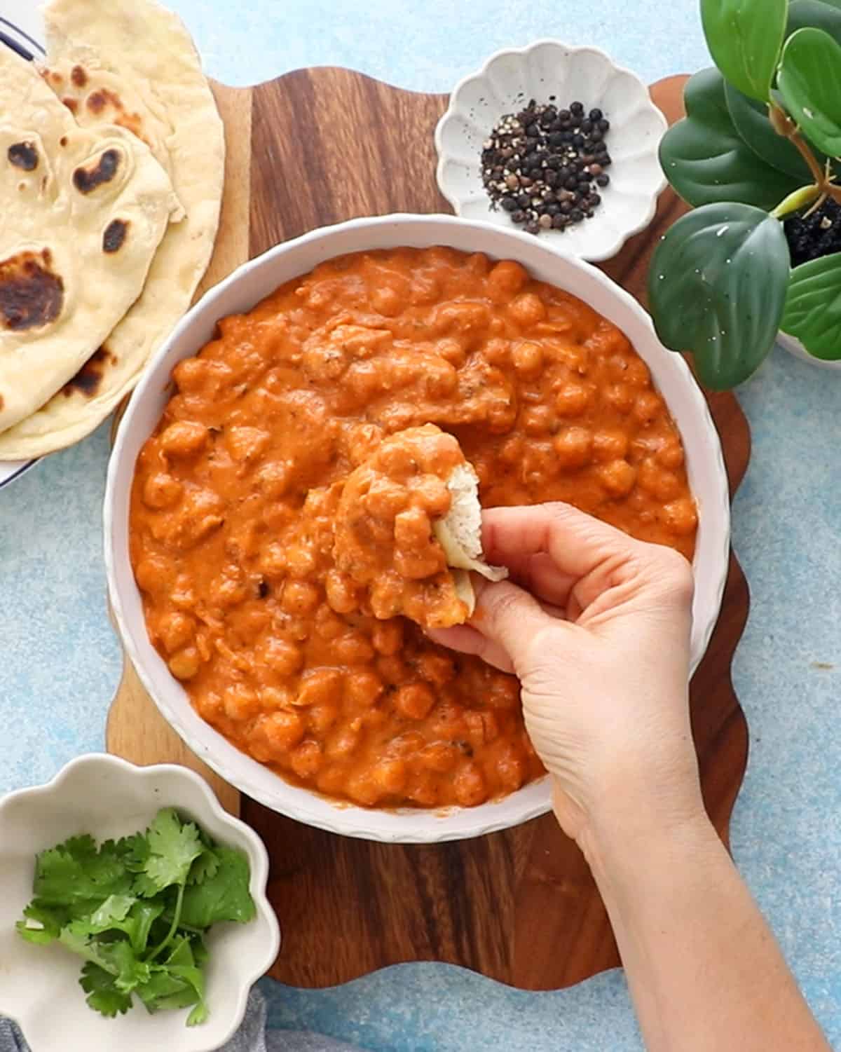a hand scooping up some orange butter chickpeas from a white bowl.